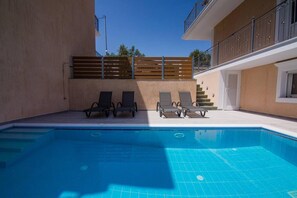 Ein Schwimmbecken mit Liegestühlen, einem Holzzaun und einer Treppe, die zu einer erhöhten Ebene führt.
