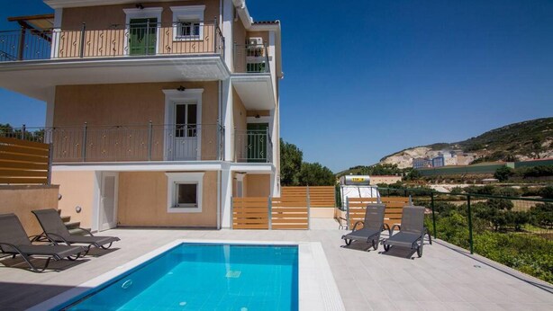 A two-story building with a swimming pool, outdoor seating, and a view of a hilly landscape. - Villa Elpida at Minies (Kefalonia)
