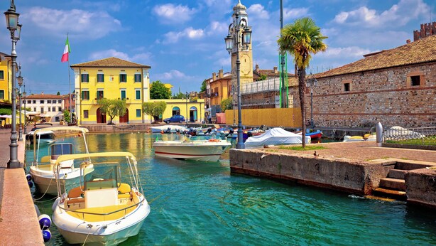 A canal with boats docked, a historic building with a tower, and a flag.