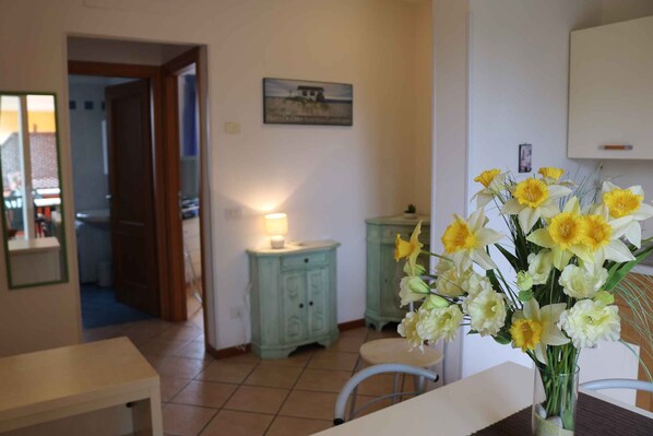 A room with a dining table, chairs, a vase with flowers, a cabinet, and a door leading to another room.