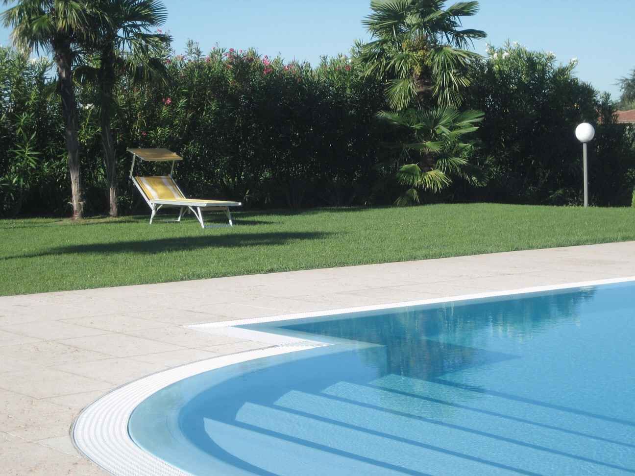 A swimming pool with a curved edge, a lounge chair, and a well-maintained lawn with palm trees.