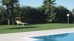 A swimming pool with a curved edge, a lounge chair, and a well-maintained lawn with palm trees.