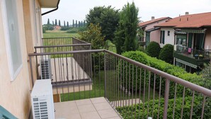 A balcony with a metal railing, a green chair, and an air conditioning unit.