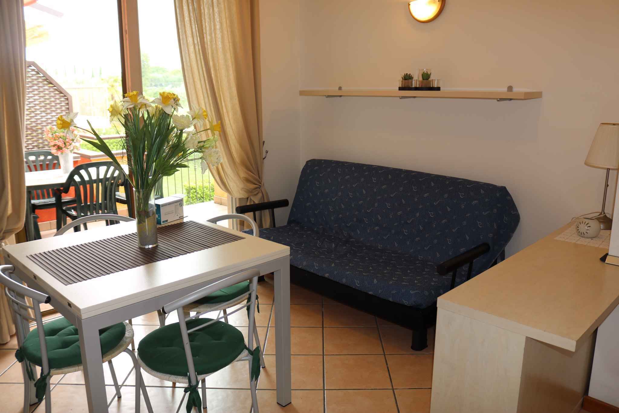 A small living area with a sofa, a dining table with chairs, a vase of flowers, and a shelf with decorative items.