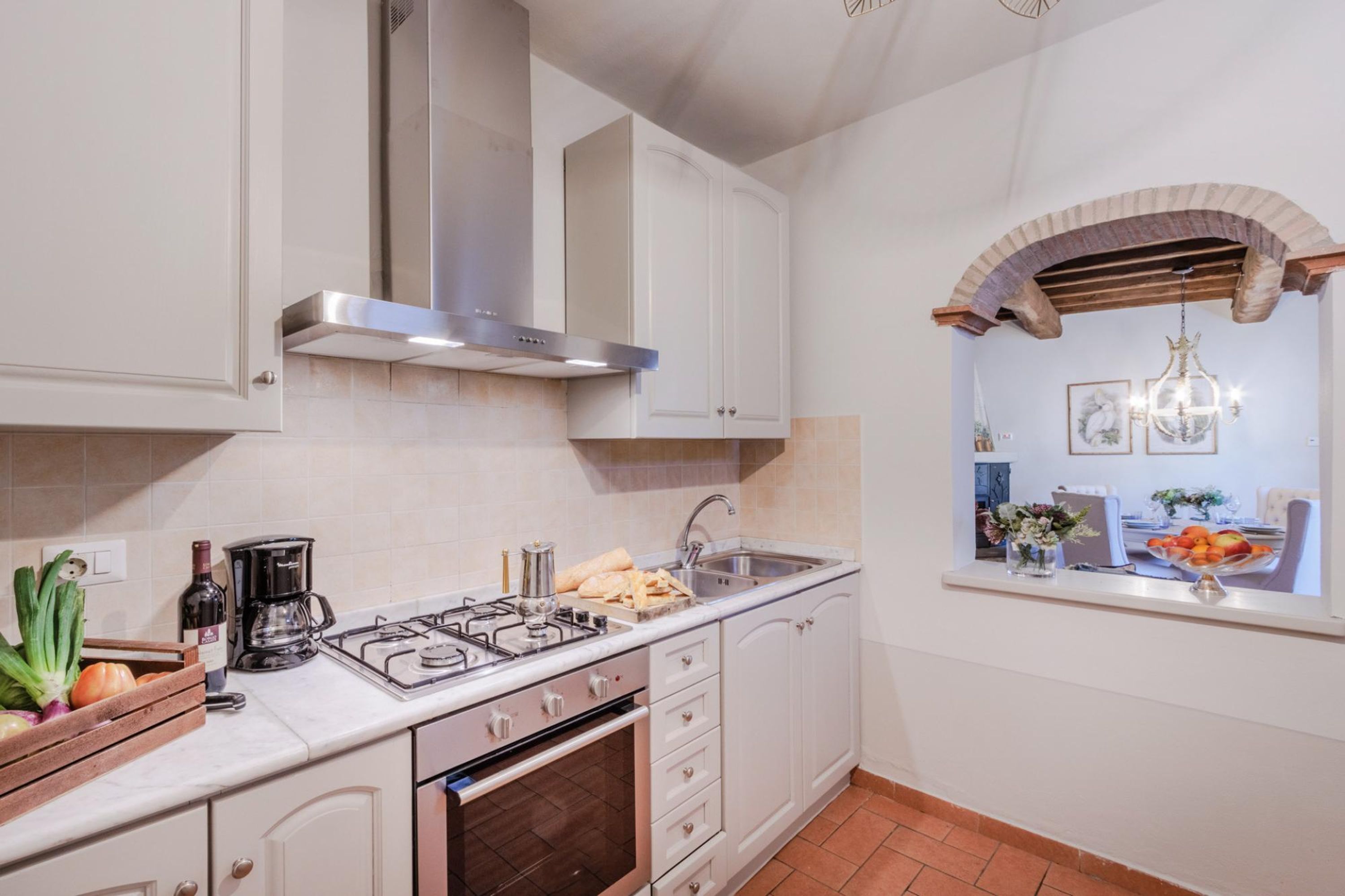 A kitchen with white cabinets, a gas stove, a stainless steel range hood, and a window with a view of a dining area.
