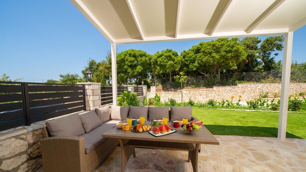 Un patio al aire libre con un sofá de mimbre, una mesa dispuesta para el desayuno y suelo de piedra.