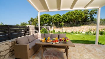 Un patio al aire libre con un sofá de mimbre, una mesa dispuesta para el desayuno y suelo de piedra.