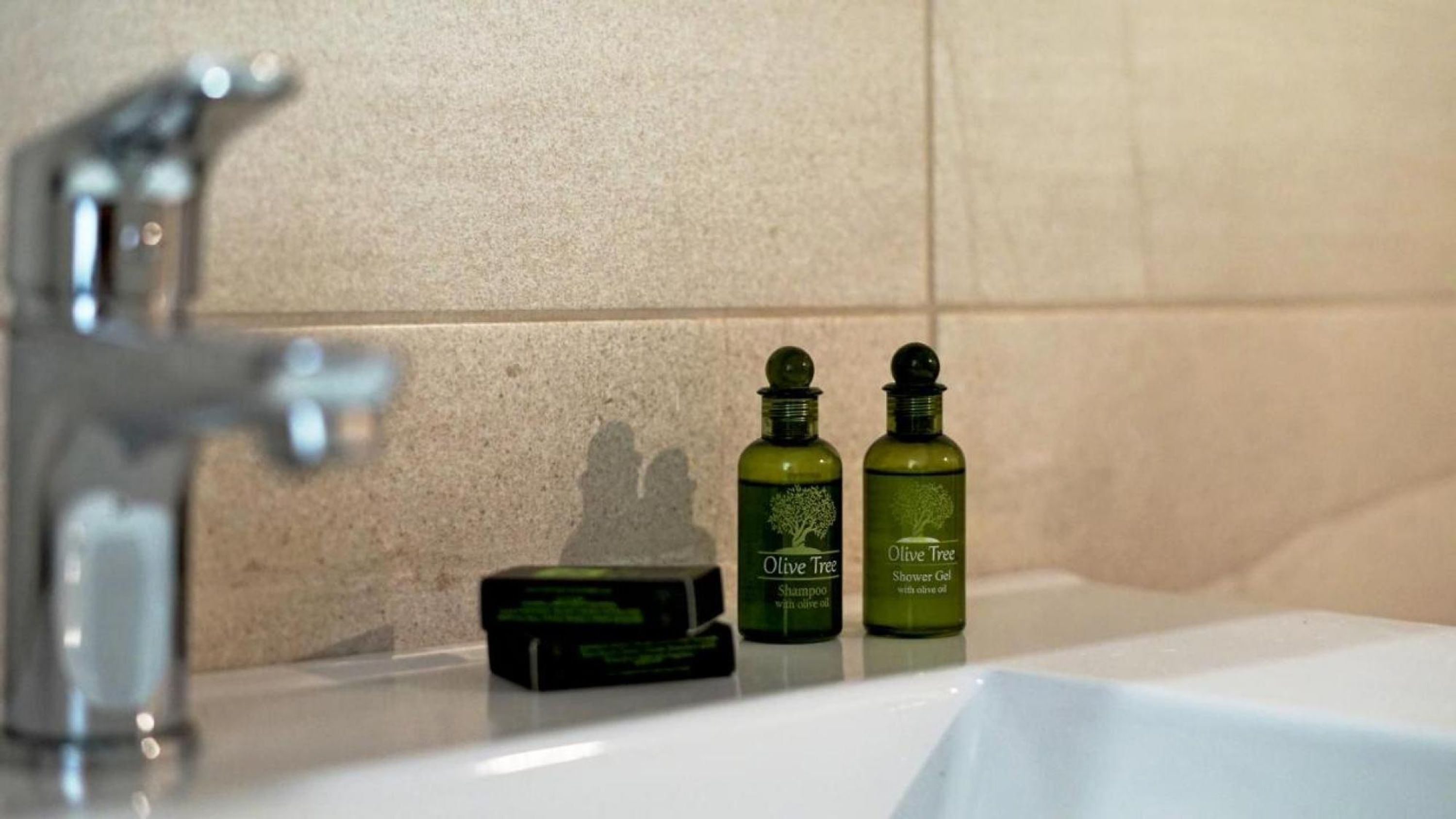 A bathroom with a sink, two bottles of Olive Tree Shower Gel, and a bar of soap.