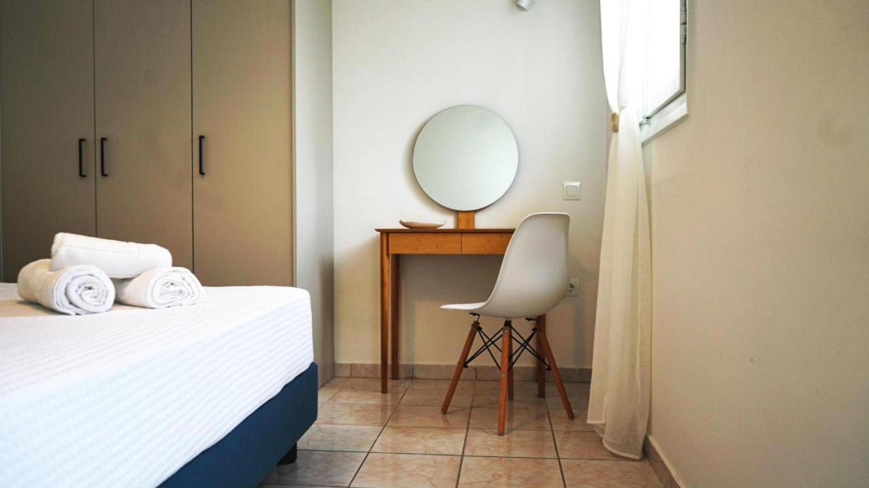 A bedroom with a bed, a desk, a chair, and a round mirror.