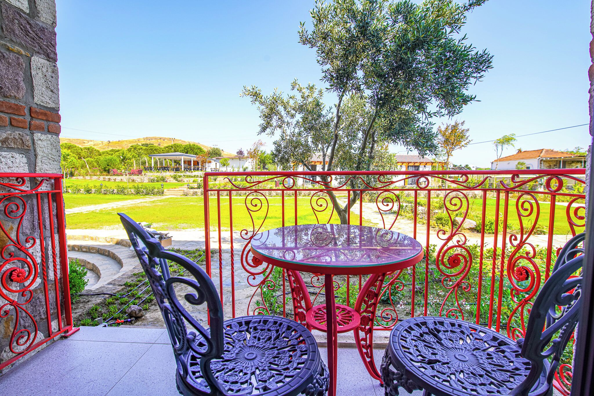 A balcony with two chairs and a table, overlooking a green landscape and a building in the distance.