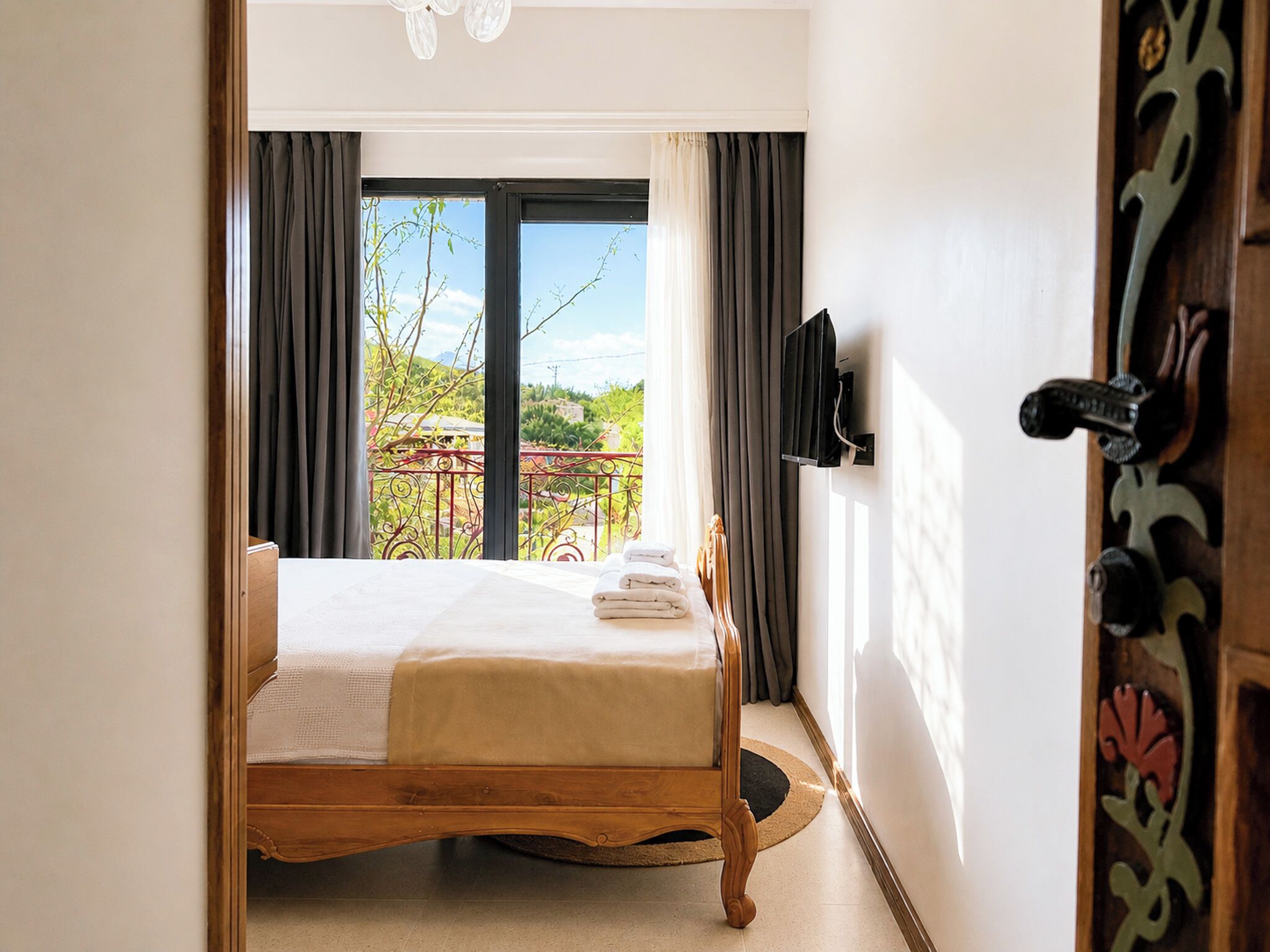 A bedroom with a wooden bed, a view of the outdoors, and a door with a decorative handle.