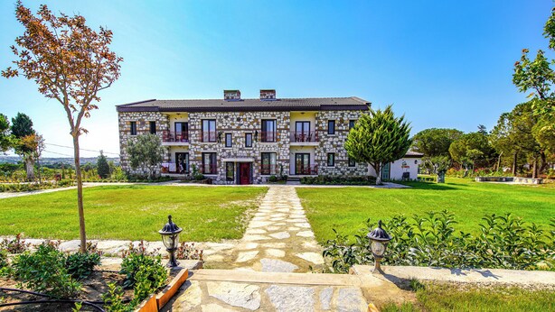 Un bâtiment en pierre avec une entrée centrale, entouré d’une pelouse et d’un jardin bien entretenus.