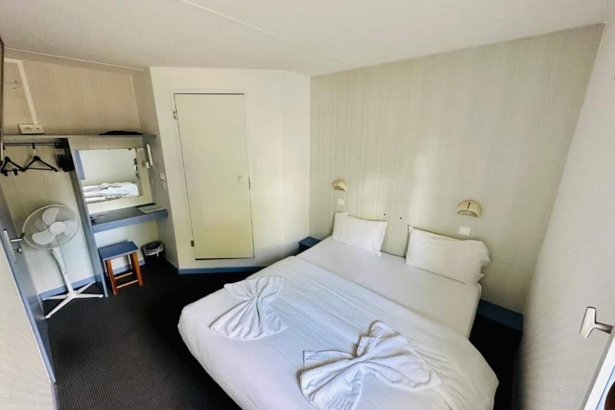 Una habitación de hotel con cama, escritorio, silla, armario, espejo, ventilador y puerta.