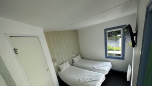 A small, single-room hotel room with two beds, a window, and a door. - Hôtel Gex (Gex)