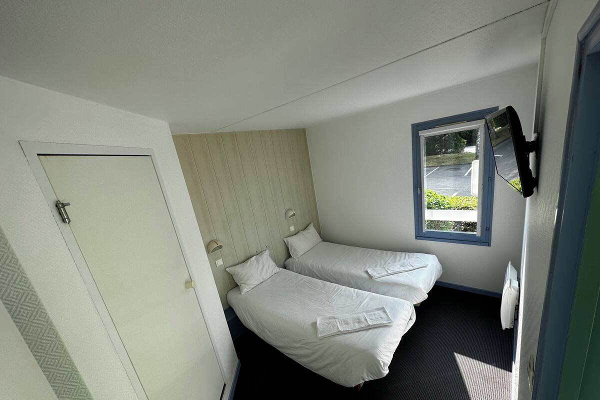 Una habitación de hotel pequeña, con dos camas, una ventana y una puerta.