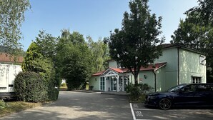 A parking lot with a building that has a red roof and a sign indicating it is a hotel. - Hôtel Gex (Gex)
