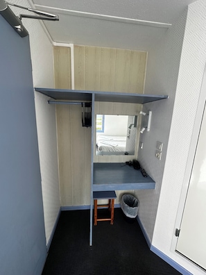 Une petite pièce comprenant un lit superposé, un petit bureau, une chaise, une poubelle et une fenêtre.