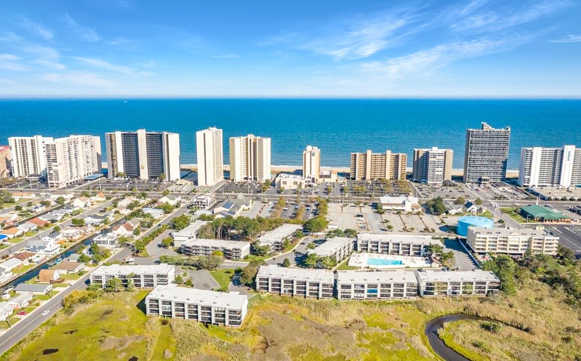 A coastal cityscape with high-rise buildings, a marina, and a clear view of the ocean.