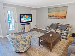 A living room with a television, a plaid sofa, a patterned armchair, and a coffee table.