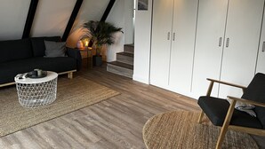 Ein modernes Schlafzimmer im Loft-Stil mit schrägem Dach, einer schwarzen Leder-Couch, einem runden Holztisch, einem schwarzen Sessel und einem großen Kleiderschrank mit Spiegelüren.