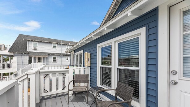 A deck with wicker chairs and a white railing, adjacent to a house with blue siding and white trim. - Cozy 1 bedroom condo, Downtown, with a pool, close to the beach and the famous OC boardwalk (Ocean City)