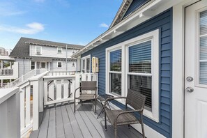 A deck with wicker chairs and a white railing, adjacent to a house with blue siding and white trim. - Cozy 1 bedroom condo, Downtown, with a pool, close to the beach and the famous OC boardwalk (Ocean City)