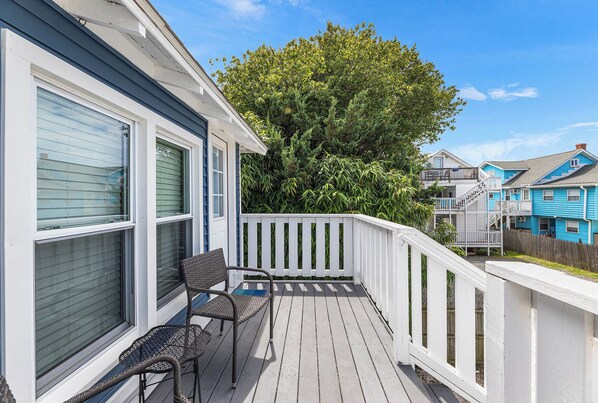 A wooden deck with two chairs, a white railing, and a large tree in the background.