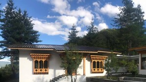 A two-story building with a stone-paved courtyard, wooden window frames, and a metal roof. - The Tiger Nest Camp (Paro)