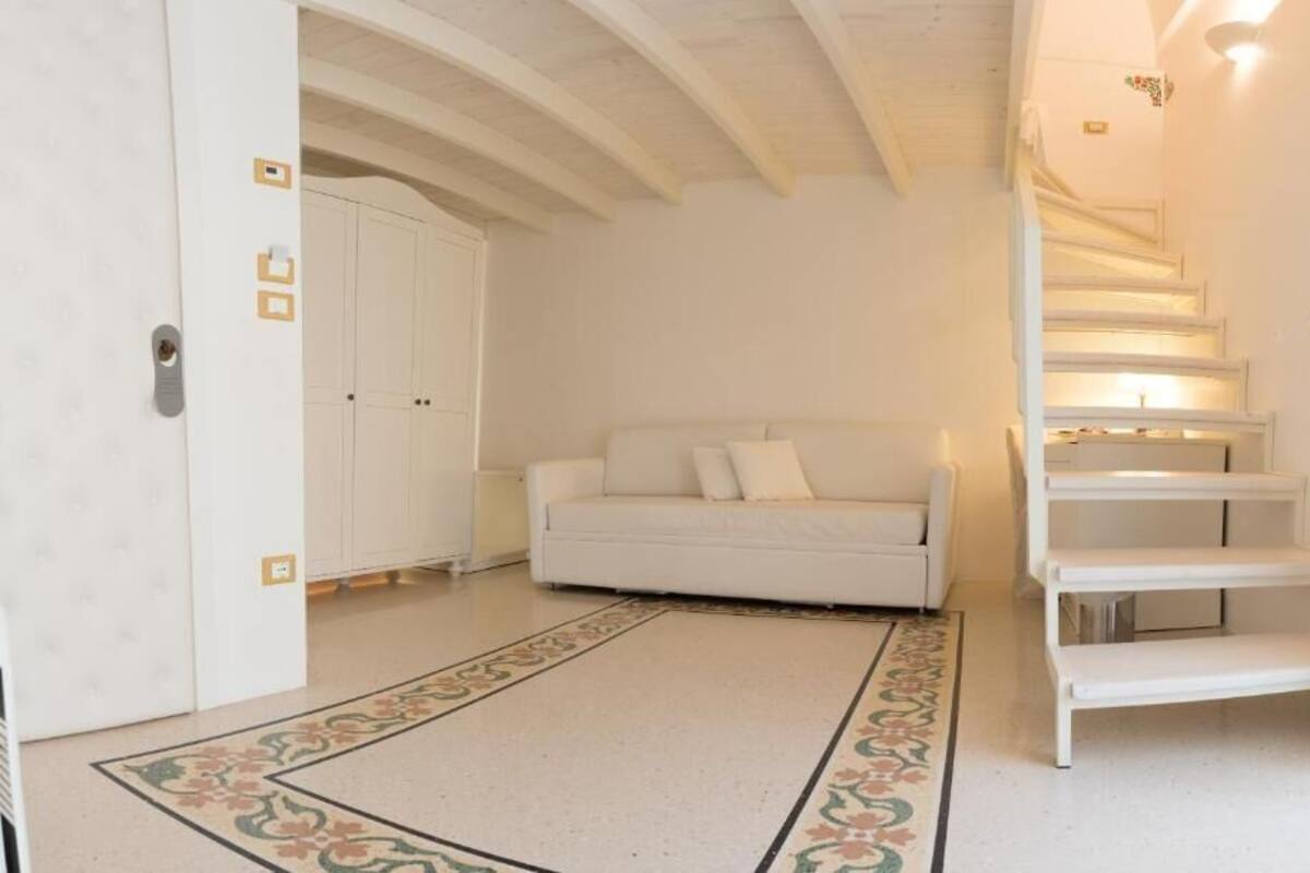 Una habitación con un sofá blanco, un tapete estampado, una escalera y un armario.