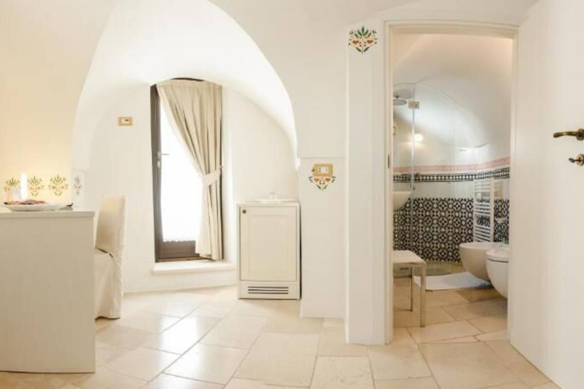 Habitación de hotel con cama, escritorio, silla, una mesita y baño visible a través de una puerta abierta.