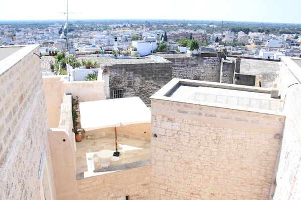 A rooftop terrace with a view of a cityscape, stone walls, and potted plants.