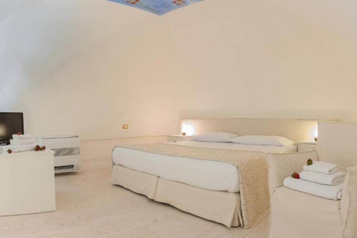 Un dormitorio con una cama grande, una mesita de noche, un televisor y un sofá blanco.