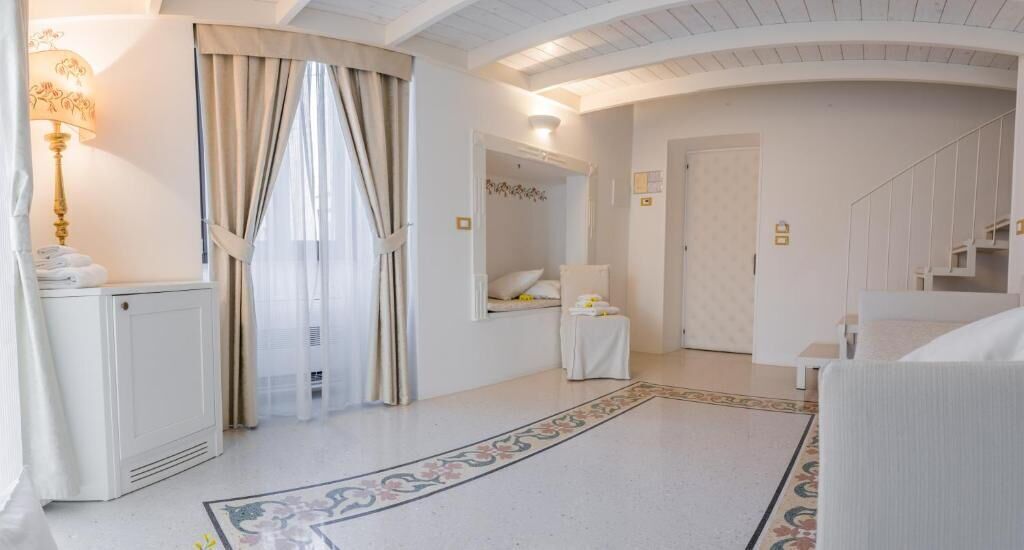 A hotel room with a bed, a bedside table, a lamp, and a window with curtains.