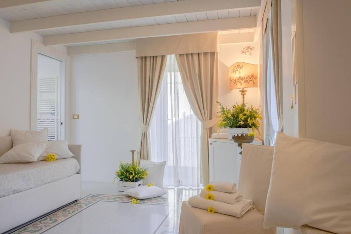 Habitación de hotel moderna y bien iluminada, con sofá, una mesita de noche con lámpara y una planta en maceta.