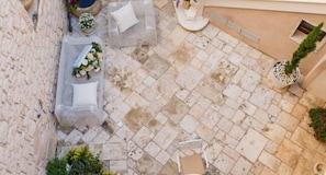 An outdoor patio with stone flooring, a seating area with a sofa and cushions, and potted plants.
