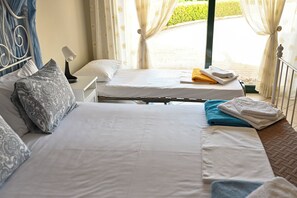 Une chambre d’hôtel avec deux lits, une table de chevet avec une lampe et une vue sur un jardin par la fenêtre.