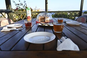 Une table en bois, dressée pour un repas, avec des assiettes, des couverts, un verre de thé, une bouteille de jus de fruits et un panier à pain.