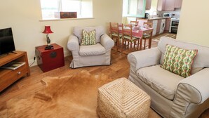 Un salon comprenant un téléviseur, un meuble rouge, deux fauteuils, un canapé et un pouf en osier tressé.