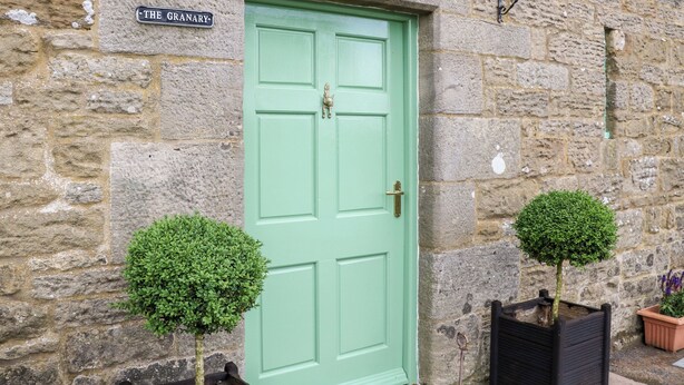 Un bâtiment en pierre avec une porte verte portant l’inscription « The Granary ». Deux petits arbres en pot sont placés devant la porte.