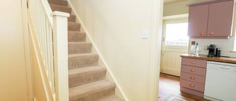A staircase leading to a kitchen with wooden flooring, a window, and a door.