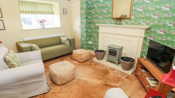 A cozy living room with a green patterned wallpaper, a fireplace, a television, and a sofa.