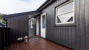 Un bâtiment moderne à l’extérieur sombre, doté d’une terrasse en bois et d’une grande fenêtre.