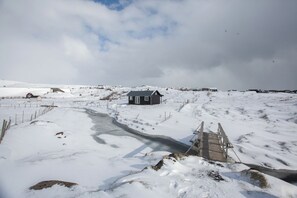 Paesaggio innevato con una piccola baita e un ponte di legno su un ruscello.