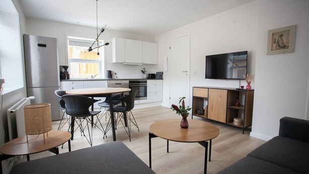 A modern kitchen with white cabinets, a dining area with a round table and chairs, a living room with a sofa, and a TV mounted on the wall. - In The Heart Of Tórshavn Nr1 (Tórshavn)