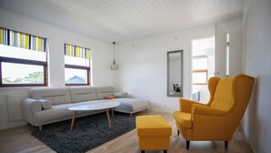 A modern living room with a sofa, ottoman, and armchair, a round coffee table, and a hanging light fixture.