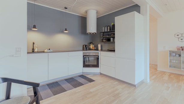 A modern kitchen with white cabinets, a built-in oven, pendant lights, and a grey rug.