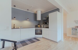 Een moderne keuken met witte kasten, een ingebouwde oven, hanglampen en een grijze vloerkleed.