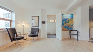 A modern room with wooden flooring, two black chairs, a floor lamp, a large map on the wall, and a view of the outside through a window.