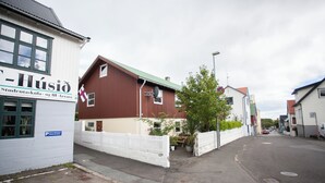 A street view with a white building labeled "Húsio" and a red building with a green roof.
