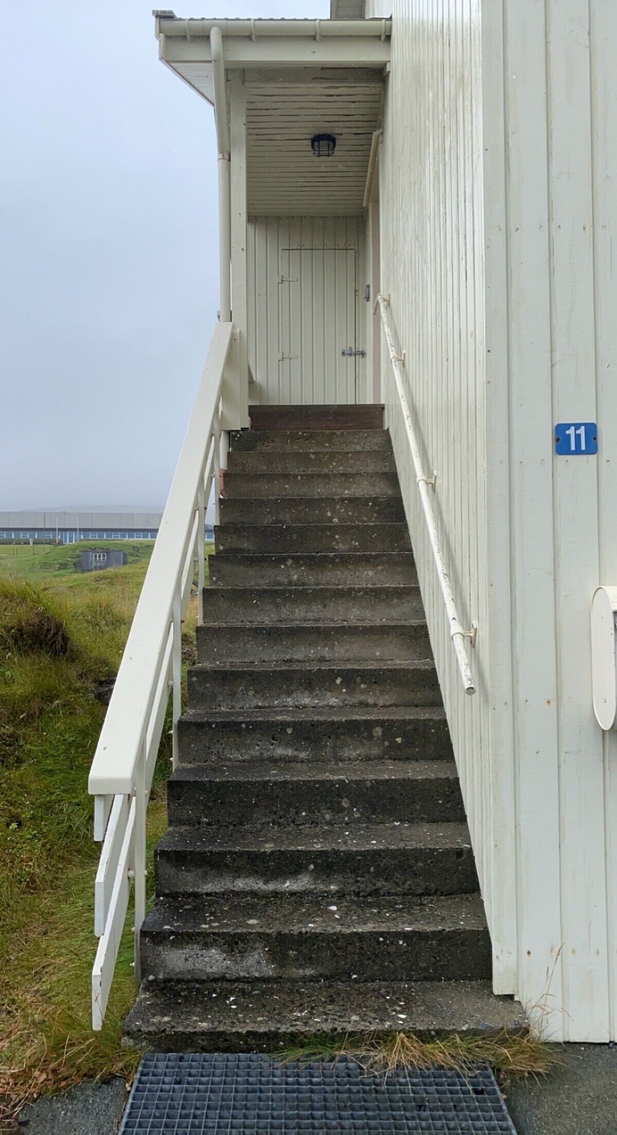 A set of concrete steps leading to a white building with a blue sign indicating the number 11.